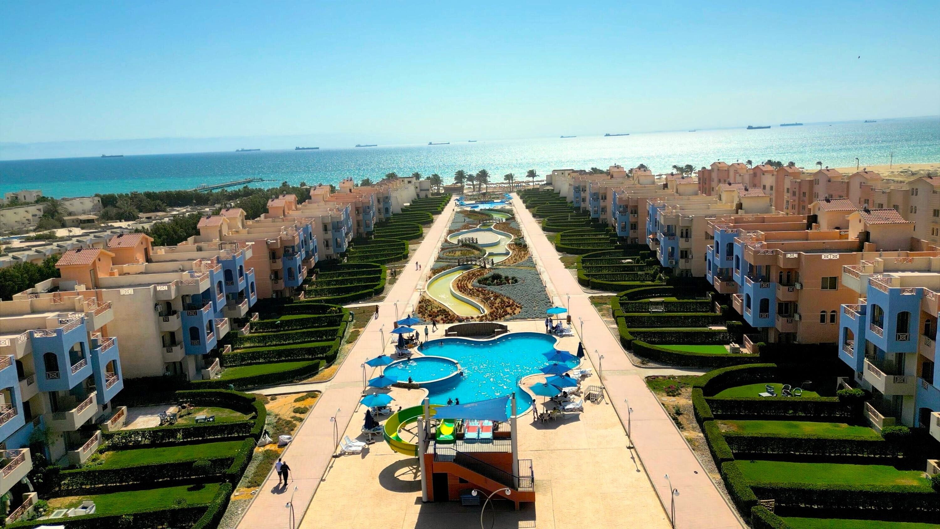 A resort with a central pool, multiple balconies, and a view of the sea.