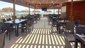 Un espacio de comedor al aire libre con mesas y sillas, techo de madera con listones, y vista a la playa y al océano.