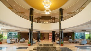 Un hall espacioso con una imponente escalera de mármol en el centro, zonas de estar y un candelabro moderno.
