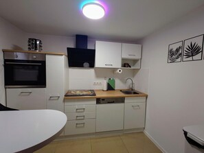 Une cuisine compacte avec des meubles blancs, un four noir, un plan de travail en bois, un lave-vaisselle et un évier.