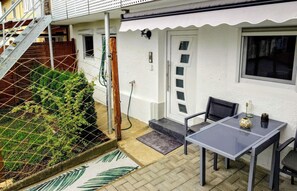 Une terrasse avec une table et des chaises, une porte et un petit espace jardin.
