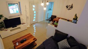 A modern living room with a flat-screen TV, wooden coffee table, dark sofa, and a dining area with a table and chairs. - Apartment Liana with Castle View (Hechingen)