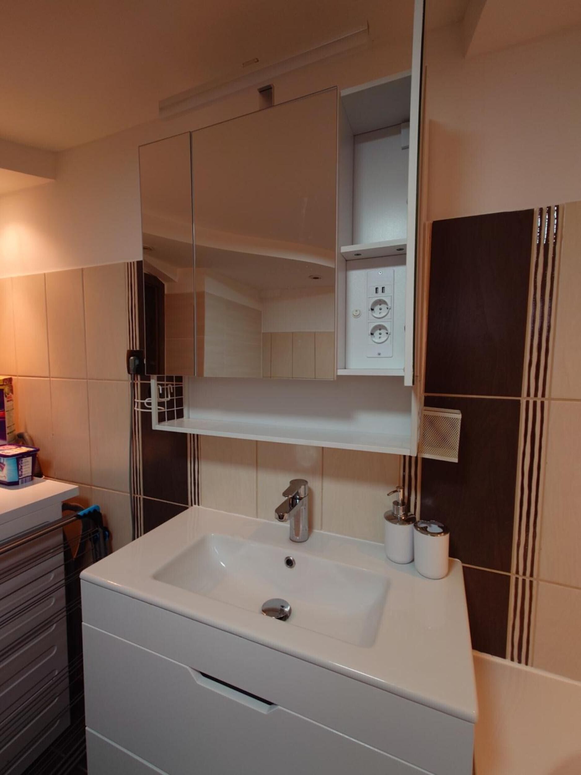 A modern bathroom with a large mirror, a white sink, and a cabinet above it.