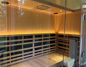 Eine Sauna mit Holzsperren und einer Glaseinteilung, einem Deckenlüftungsgitter und einer Sitzbank.
