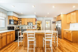 A modern kitchen with wooden cabinets, stainless steel appliances, and a central island with chairs. - Ludlow Village Farmhouse - Indoor Sauna; on Shuttle Route, Steps from Downtown!🎉 (Ludlow)