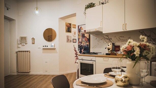 Et moderne køkken med hvide skabe, et rundt spejl og et spiseområde med et bord dækket til to.