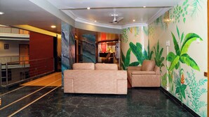 A lobby with a marble floor, a sofa, a chair, and a wall with tropical plant murals. - Dhammanagi comforts (Hubli)