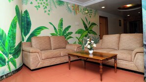 A living room with two sofas, a wooden coffee table, and a wall mural of tropical leaves. - Dhammanagi comforts (Hubli)