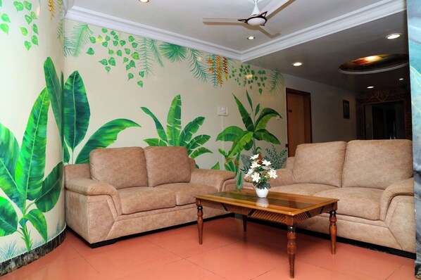 Una sala de estar con dos sofás, una mesa de centro de madera y un mural de hojas tropicales.