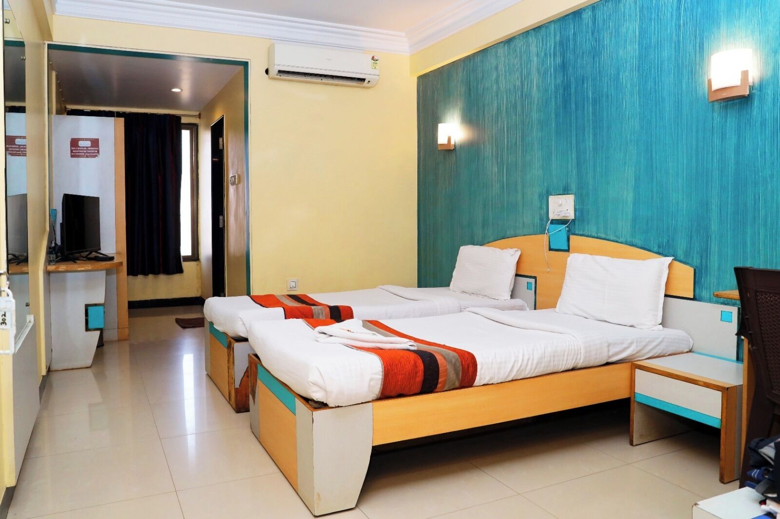 Una habitación de hotel con una cama, mesitas de noche, un aire acondicionado y una televisión.