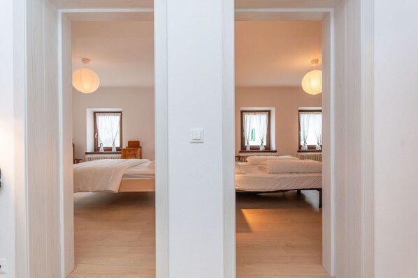 Un lungo corridoio con specchi che porta a due camere da letto identiche, con pavimento in legno, comodini e una finestra con tende.