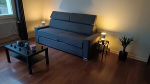 Ein Wohnzimmer mit einem dunkelblauen Sofa, einem kleinen schwarzen Tisch mit Kerzen und einer Topfpflanze.