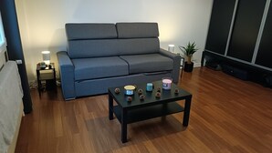 Ein Wohnzimmer mit grauem Sofa, einem schwarzen Couchtisch mit Kerzen und einer kleinen Pflanze.