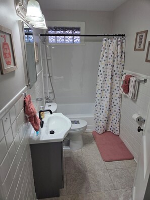 A bathroom with a white sink, toilet, and bathtub. There is a shower curtain with a polka dot pattern, a pink bath mat, and a towel rack with a towel. - Cozy 1-bedroom building in terrific Springfield with AC (Springfield)
