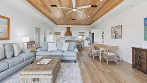 A spacious living room with a grey sofa, a coffee table, and a dining area with wicker chairs. - Beach House - Walking on Water by PHG (St. George Island)
