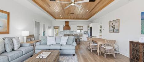 A spacious living room with a grey sofa, a coffee table, and a dining area with wicker chairs.