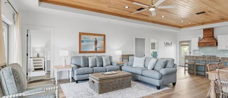 A spacious living room with a large sectional sofa, a wicker coffee table, and a dining area with a wooden table and chairs.
