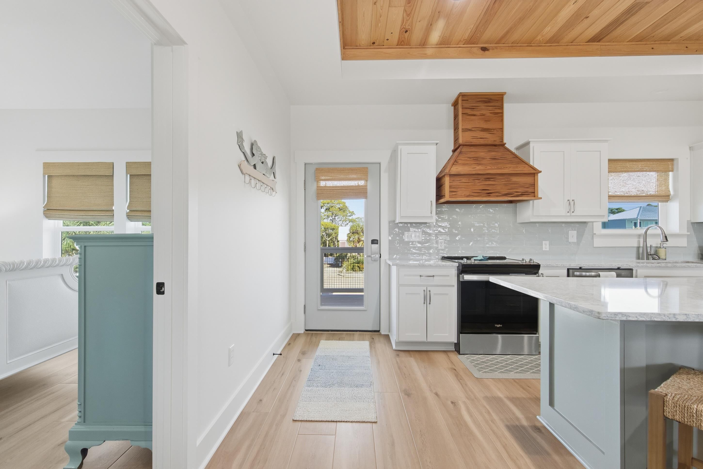 Een moderne keuken met witte kasten, een houten plafond en een uitzicht door de deur.