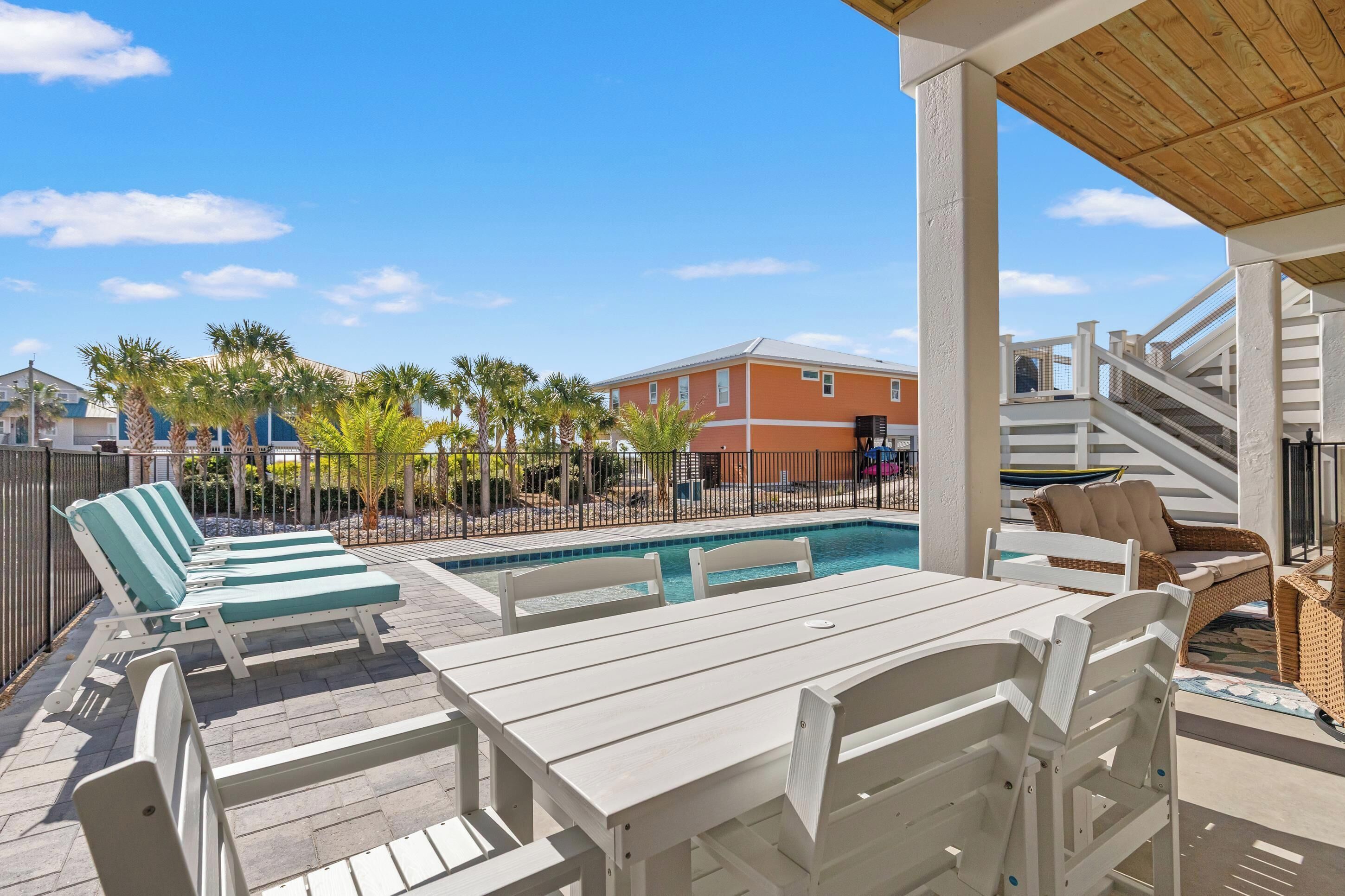 A poolside area with lounge chairs and a table, a wooden pergola, and a view of a building in the background.