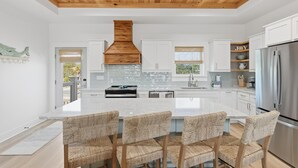 A modern kitchen with a central island, white cabinetry, and a stainless steel refrigerator. - Beach House - Walking on Water by PHG (St. George Island)