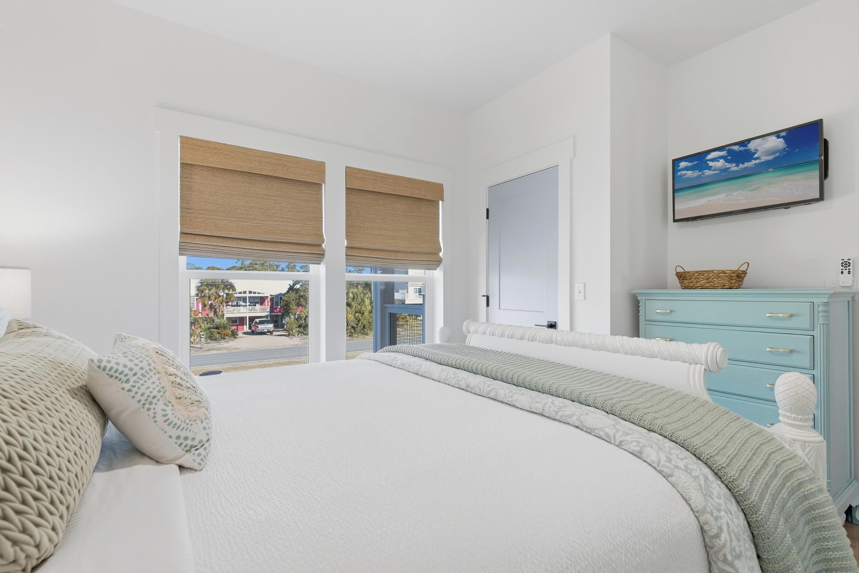 A bedroom with a large bed, a dresser, a television, and a window with blinds.