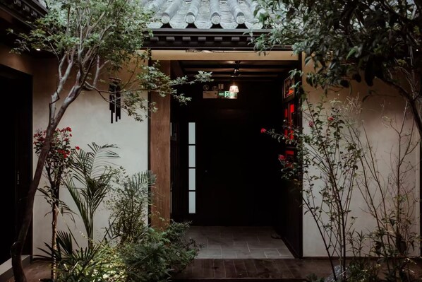 A traditional Japanese-style entrance with a tiled roof, a wooden door, and a small garden area with various plants and a stone pathway. - WUTA Designer Hotel (Chaozhou)
