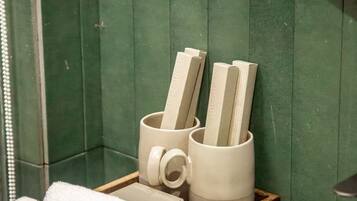 A bathroom with green tiles, a wooden tray holding towels and a toothbrush, and a sink.