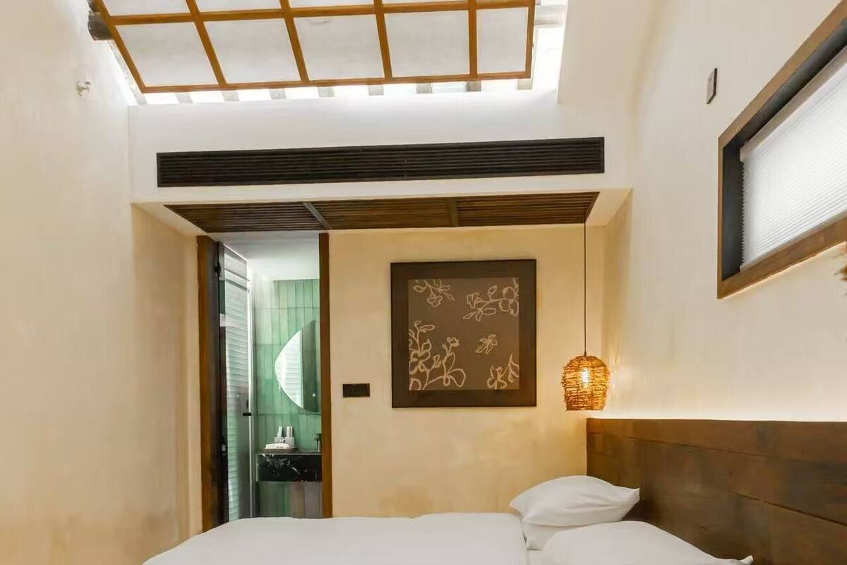 A bedroom with a large bed, a wooden headboard, a wall-mounted light fixture, and a door leading to a bathroom.