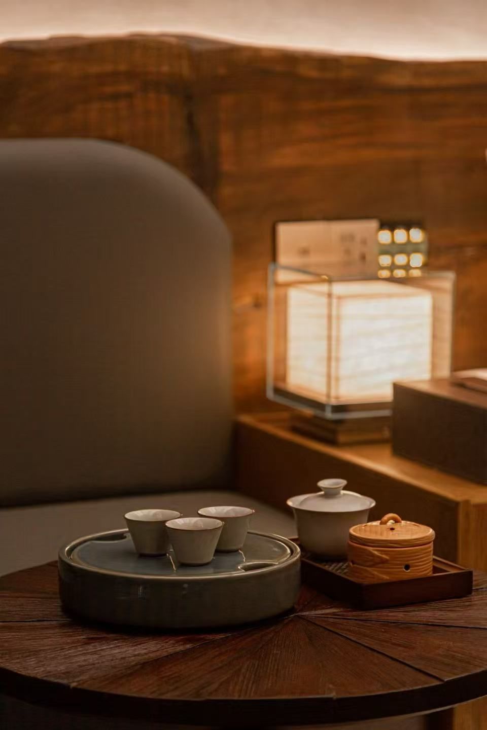 A cozy seating area with a round wooden table, a cushioned chair, and a small table lamp.