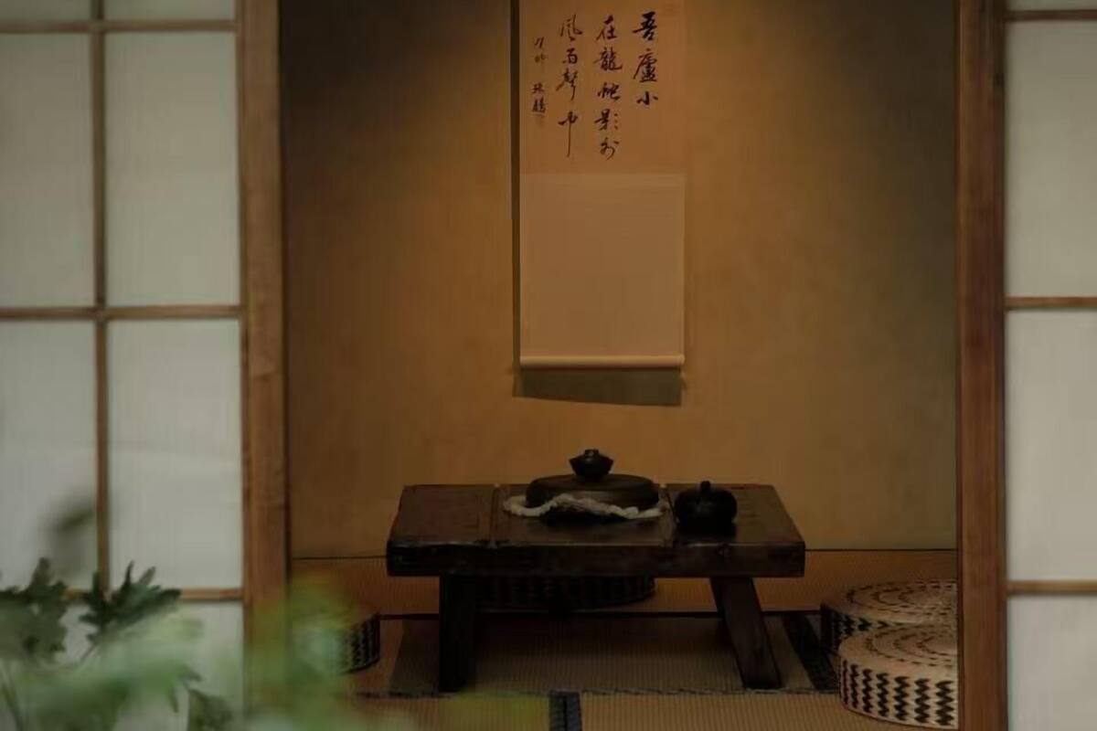 A traditional Japanese room with tatami flooring, a shoji screen door, a small table with a tea set, and a hanging scroll with calligraphy.