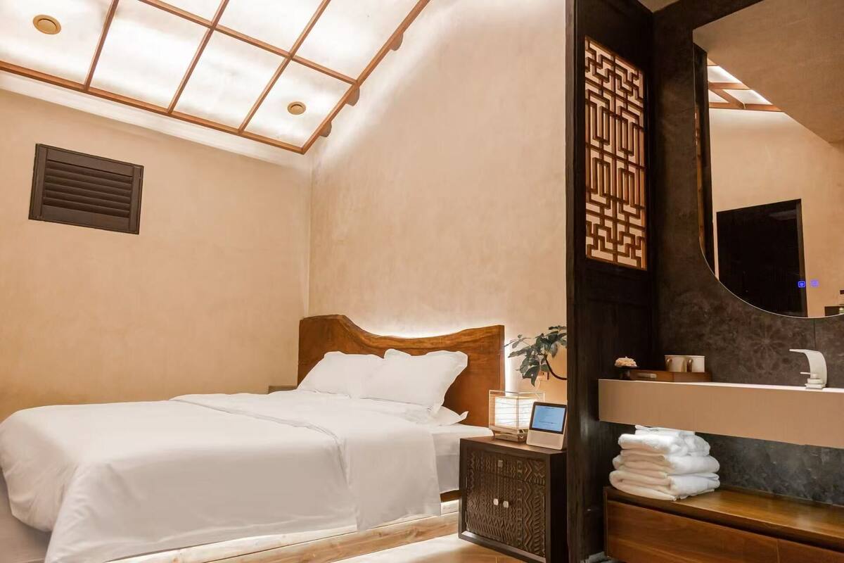 A hotel room with a bed, bedside table, and a mirror.