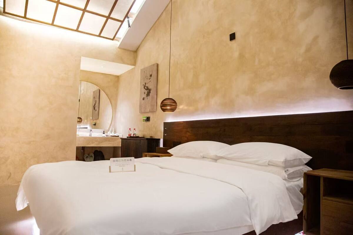 A hotel room with a large bed, a bedside table, a nightstand, a mirror, and a ceiling light fixture.