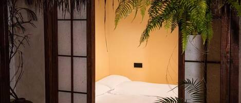 Una habitación con cama, ventana con vista a una planta y pared con textura.
