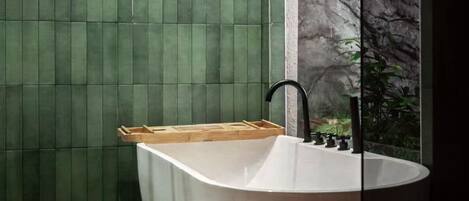A modern bathroom with a freestanding bathtub, green tiled walls, and a window with a rocky backdrop.