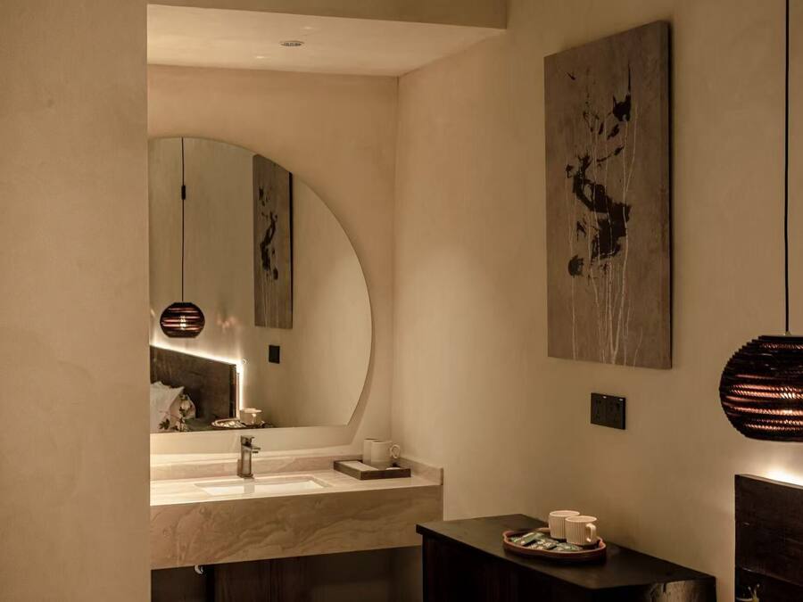 A modern bathroom with a large mirror, a sink, and a small table with toiletries.