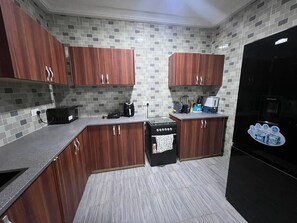 A kitchen with wooden cabinets, a black stove, and a tiled backsplash. - Spacious 5-bedroom apartment in serene Haatso Atomic Road with AC (Haatso)