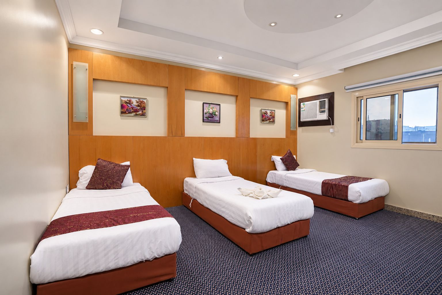 Quarto de hotel com três camas, uma janela grande e obras de arte nas paredes.