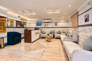 A reception area with a marble floor, sofas, a reception desk, and a television. - MG Crown Hotel 3 (Madinah)