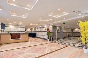 Een hotel lobby met een receptiebalie, zithoek en een plant.