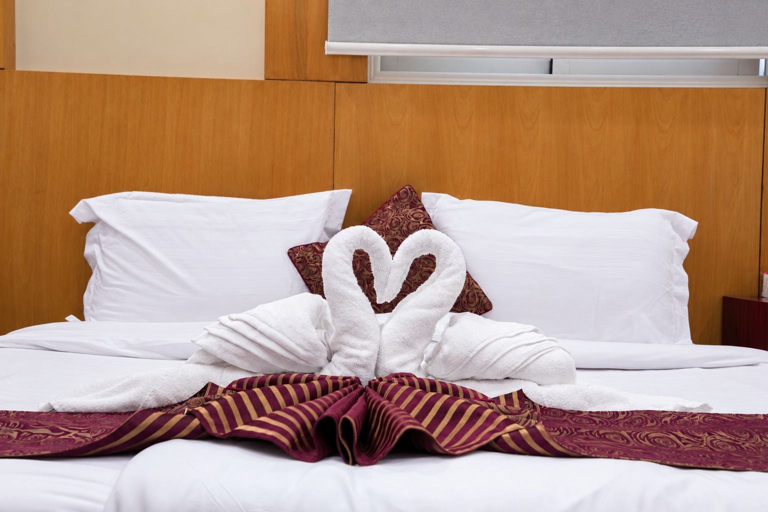 Quarto de hotel com cama bem arrumada, travesseiros brancos, arranjo de toalha em forma de cisne e manta listrada.
