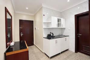 Una habitación de hotel con kitchenette, un armario de madera, una encimera negra y una pared de mármol.