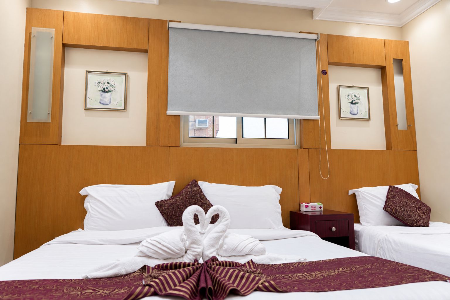 Habitación de hotel con cama, dos almohadas, mesita de noche y ventana con persianas.