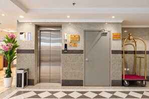 Een lift, een deur en een karretje met een rood kussen in een ontvangstruimte.