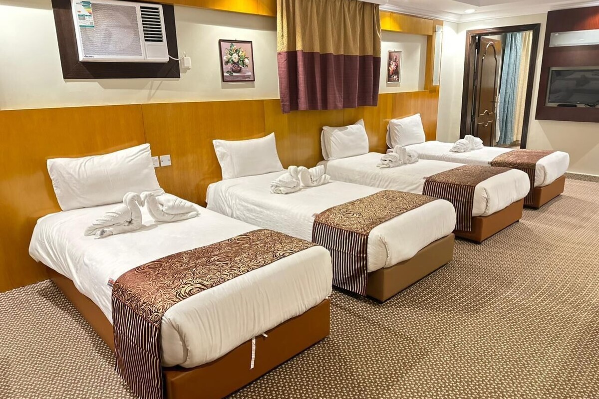 A hotel room with four beds, a large air conditioning unit, a television, and a mirror.
