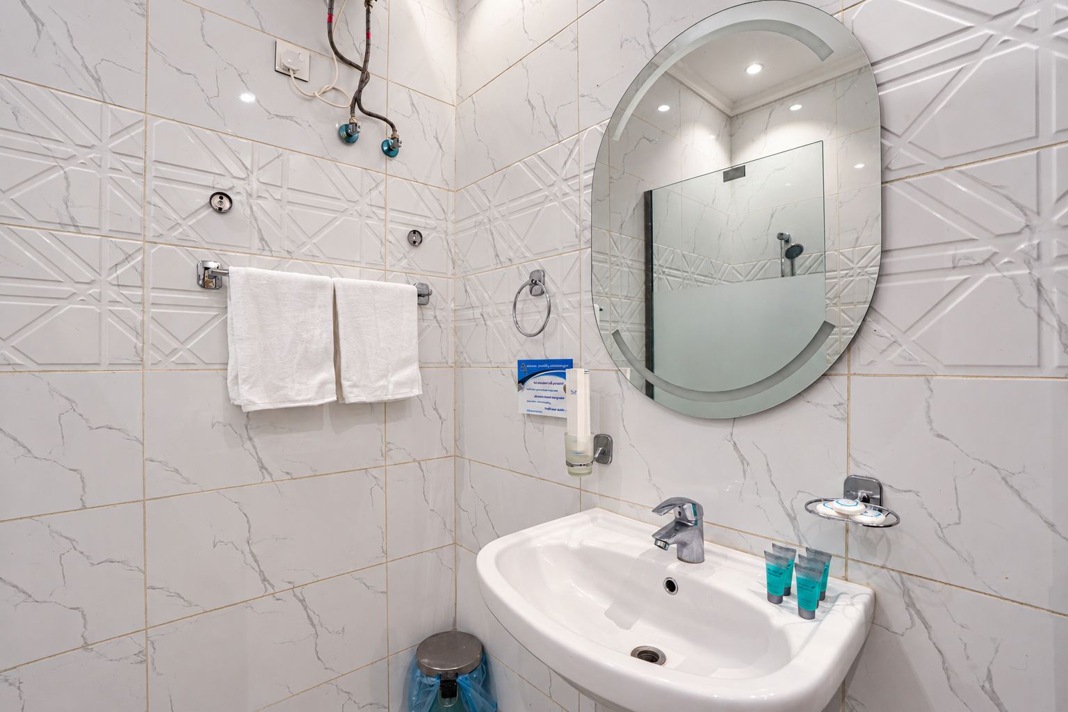 Ein Badezimmer mit Wand in Marmoroptik, einem weißen Waschbecken, einem Spiegel und einem Handtuchhalter.