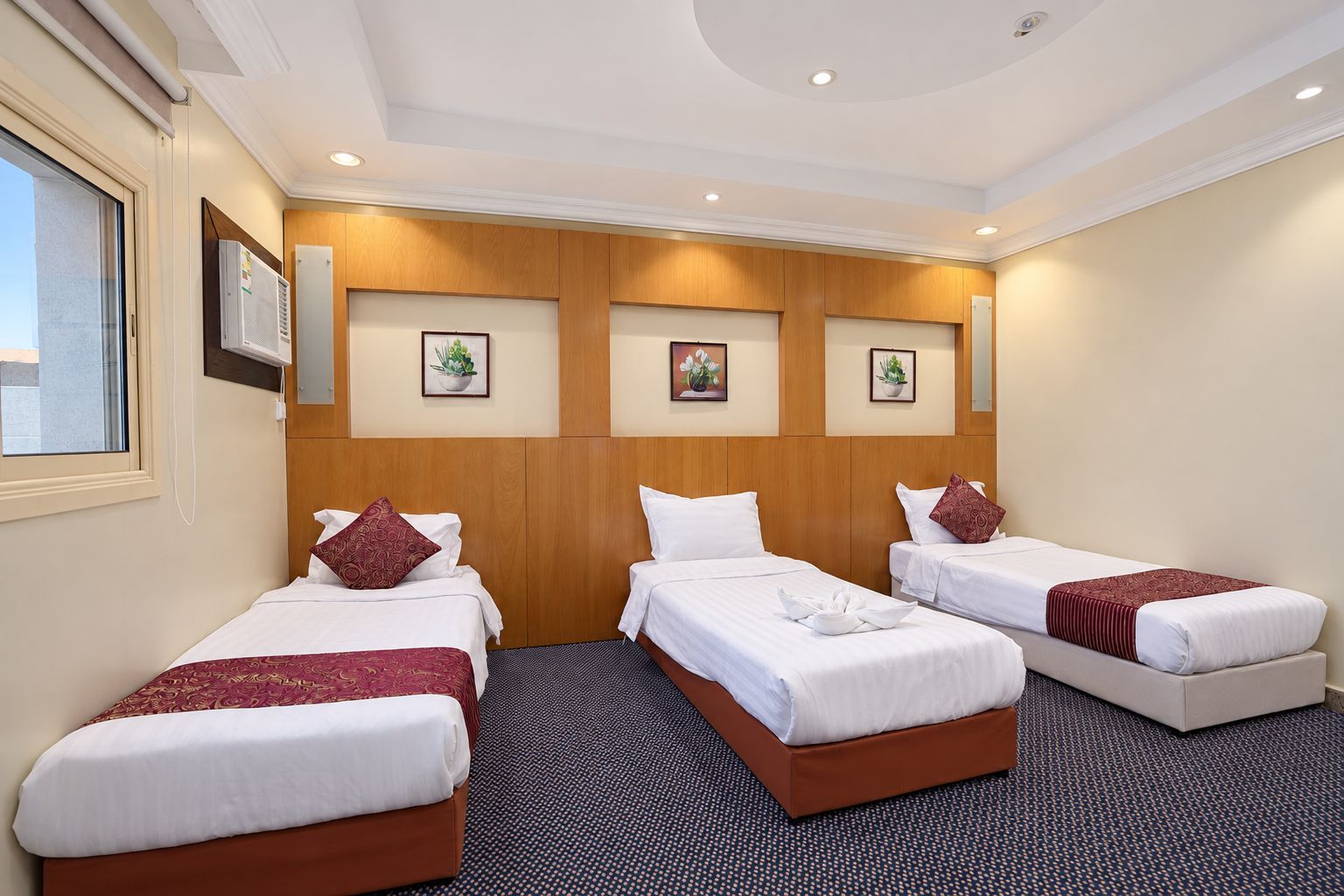 Ein Hotelzimmer mit drei Einzelbetten, einem Holz-Kopfteil und einem Fenster.