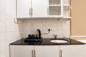 Una cocina con encimera negra, armarios blancos, una cafetera y un lavabo.