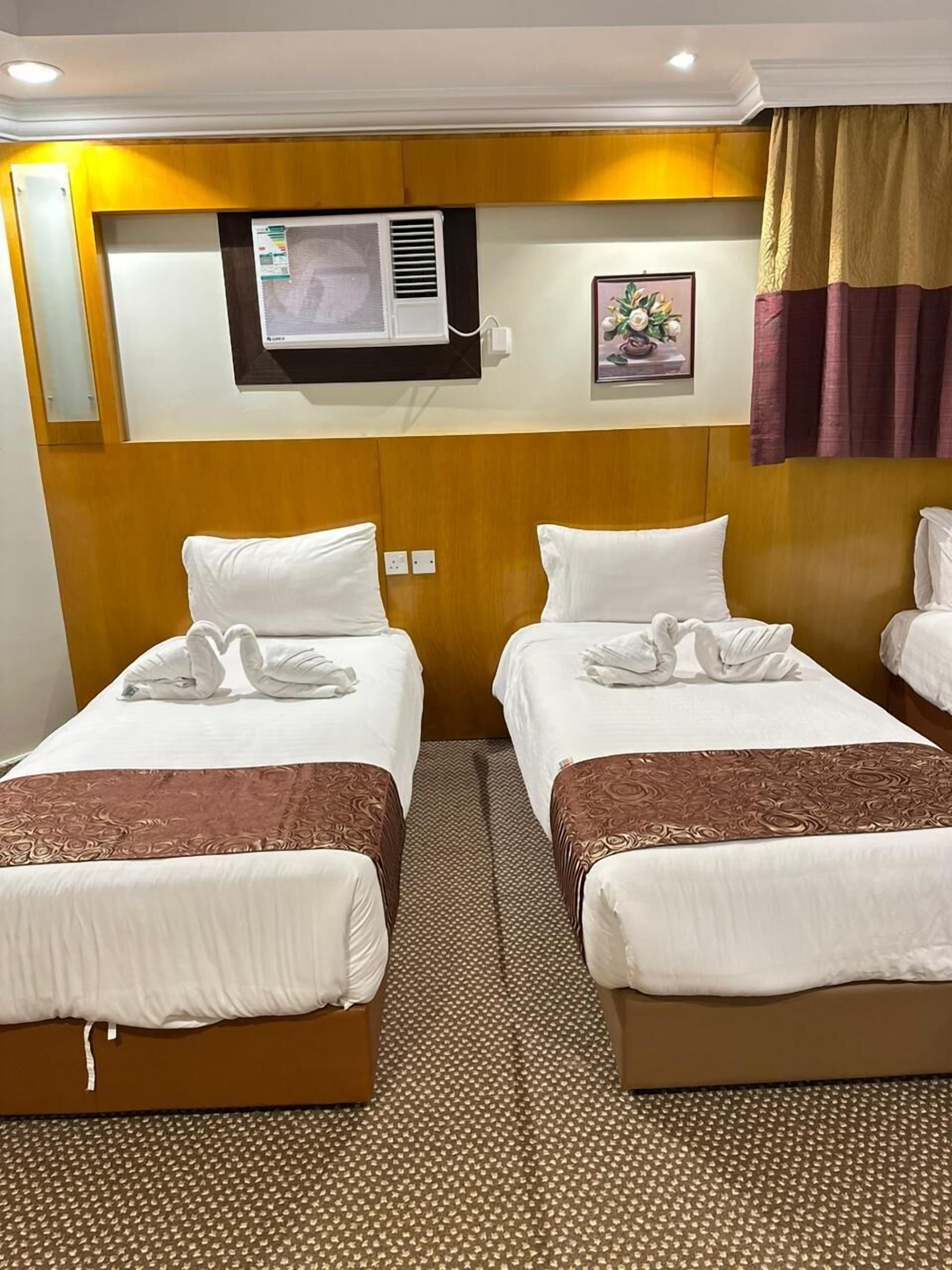 Hotelkamer met twee bedden, een wandairconditioner, een klein schilderij en een raam met gordijnen.