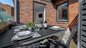 A dining table set with plates, glasses, and cutlery, a bottle of wine, and a pitcher of water, against a brick wall with a window and a door. - Stadtperle Gold in the heart of Westerland with roof terrace and close to the beach (Sylt)