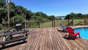 A wooden deck with a barbecue grill, picnic table, and red chairs by a swimming pool. - Stunning and private lake front sunrise and sunset views! (Nevada)